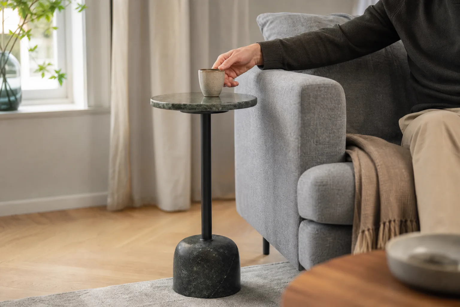 Runt sidobord med stenskiva intill grå soffas armstöd
